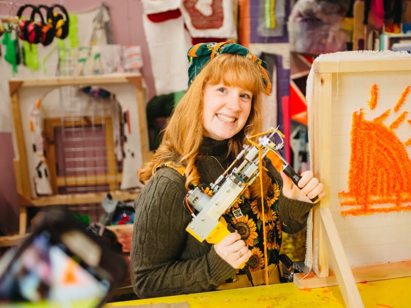 A woman poses with a tufting gun
